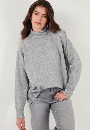 Light gray, oversized turtleneck sweater in soft knit fabric with ribbed cuffs, paired with matching gray jeans. Simple, contemporary design.