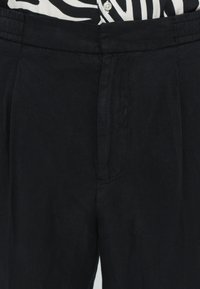 Zwarte geplooide broek met een gladde textuur, elastische tailleband en zijzakken. De stoffen lijken lichtgewicht en comfortabel.