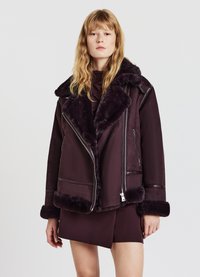 Giacca di shearling bordeaux con colletto in pelliccia sintetica, chiusura con zip e dettagli a contrasto. Presenta una vestibilità comoda e una texture morbida.