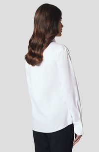 Biała koszula z długim rękawem, wykonana z gładkiego materiału, z klasycznym kołnierzykiem, zaokrąglonym dołem i zapinanymi mankietami. Widok z tyłu ukazuje elegancki design.