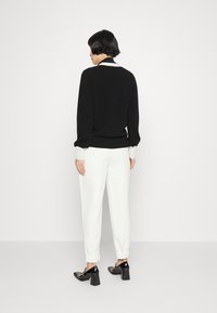 Sweater preto com colarinho branco, punhos brancos e bainha elástica, combinado com calças brancas ajustadas e sapatos de salto bloco pretos.