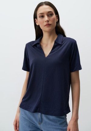 Polo shirt bleu marine à manches courtes avec un décolleté en V et une coupe décontractée, fabriqué en tissu léger et doux. Il présente une texture lisse et un design décontracté.
