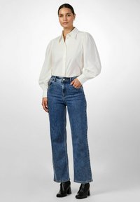 Valkoinen puffi-hihat-paita nappisuljennalla, yhdistettynä korkeavyötäröisiin sinisiin suoriin farkkuihin ja mustiin korollisiin nilkkureihin.