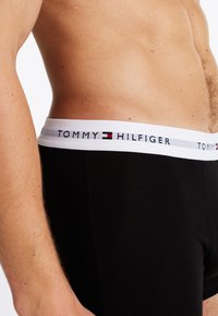 Sorte bomull boxershorts med en hvit elastisk linning som har "TOMMY HILFIGER" logo i blå og rød tekst.