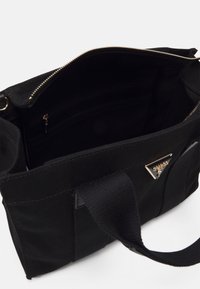 Sac à main en tissu noir avec fermeture éclair ouverte sur le dessus, poche intérieure zippée et double poignée, avec une petite plaque logo triangulaire en métal.
