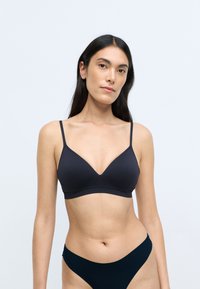 Bra wireless nero con scollo a V, spalline sottili e tessuto liscio. Abbinato a un bikini bottom scuro coordinato.