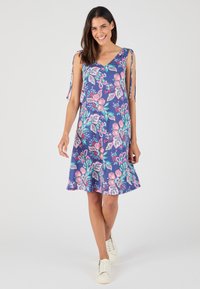 Robe florale en tissu bleu, avec un décolleté en V, des bretelles réglables et un ourlet évasé orné de motifs roses et verts. Assortie avec des baskets blanches.