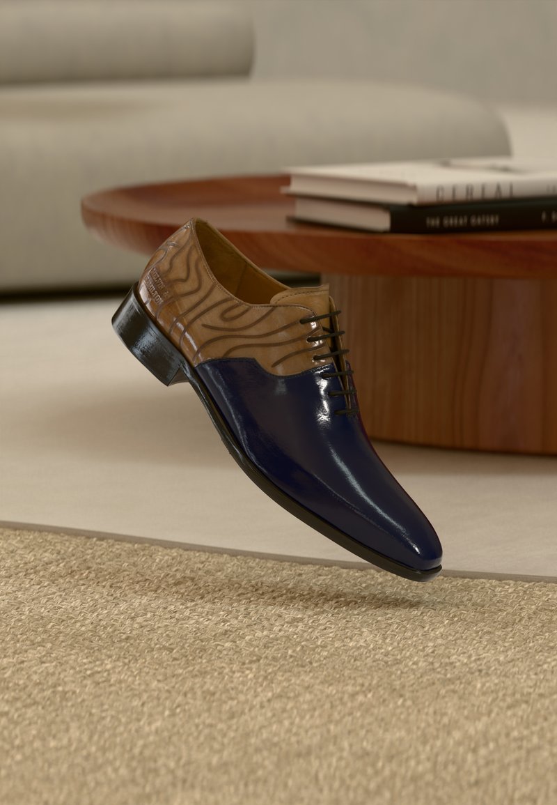 Καφέ δέρμα με κυματοειδές μοτίβο, μπλε γυαλιστερή μύτη, δέσιμο με κορδόνια και μαύρη σόλα. Το παπούτσι αιωρείται πάνω από μια υφασμένη μπεζ επιφάνεια.