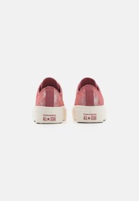 Baskets Converse en suédine rouge avec une finition texturée, semelles en caoutchouc blanc et logo "ALL STAR" en relief au talon.