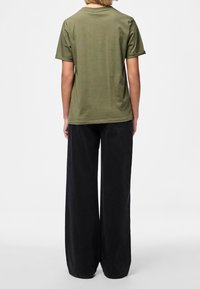 Olivově zelené tričko s krátkým rukávem a kulatým výstřihem, v kombinaci s volnými černými kalhotami s širokými nohavicemi, které mají jemnou texturu a detaily stehování.