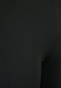 Leggings neri realizzati in un materiale liscio ed elastico. Presentano un design semplice con una finitura senza cuciture e senza hardware o motivi visibili.