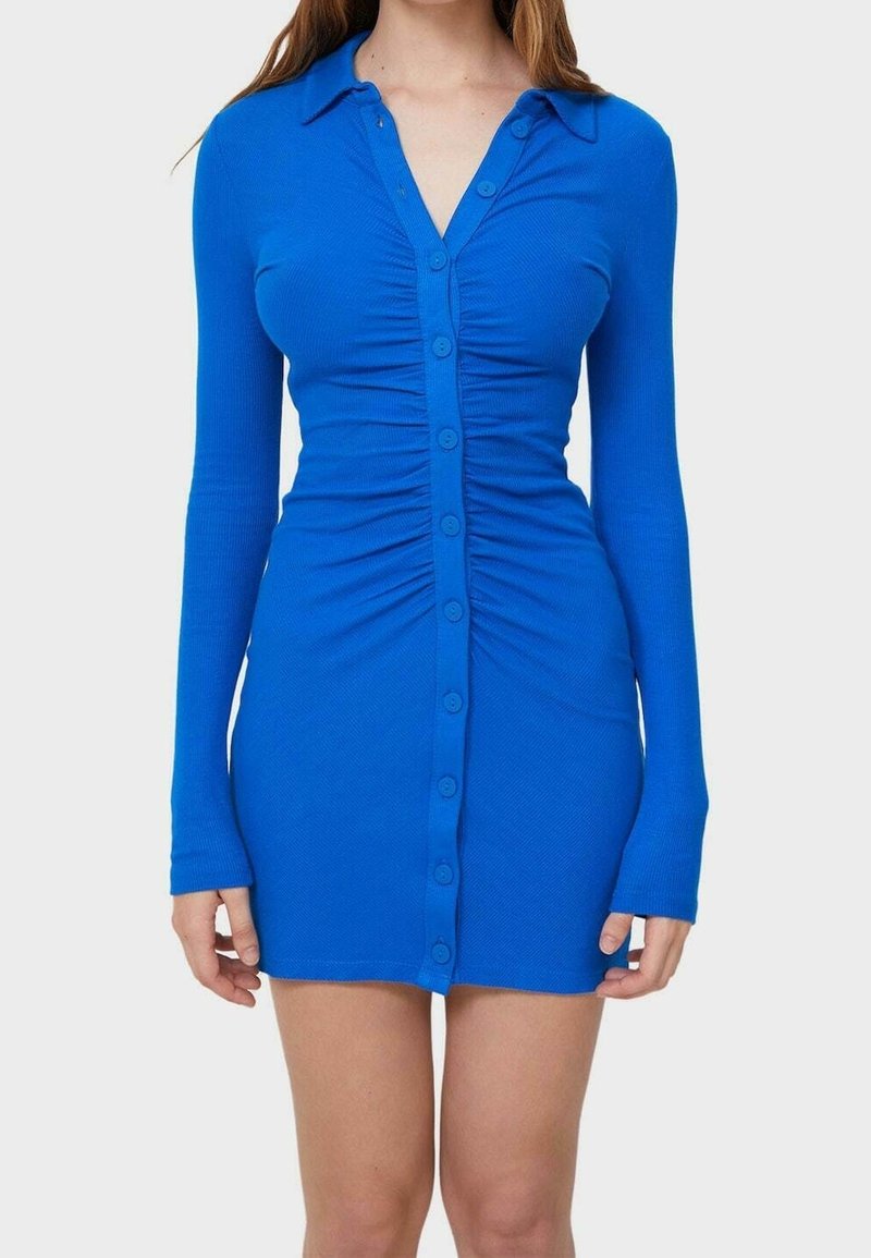 Robe bleue côtelée à boutons avec une silhouette ajustée, des manches longues et des détails froncés à l'avant. Texture douce et design avec col.