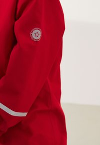 Manche de veste rouge avec bande blanche réfléchissante et emblème circulaire représentant une étoile avec le texte « I AM THE FUTURE » sur le haut du bras.