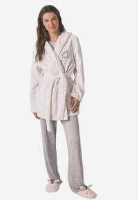 Witte pluche badjas met een ceintuurriem, voorzien van een konijn-afbeelding. Gecombineerd met grijze broek met luipaardprint en beige pantoffels met konijnengezichten.