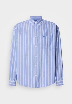 Camisa azul clara com listras verticais brancas, mangas compridas, um bolso no lado esquerdo do peito e uma pequena etiqueta com logótipo.