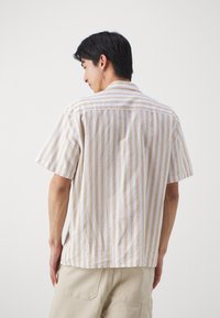 Camisa de manga corta en rayas verticales beige y blancas, hecha de tejido ligero con un corte holgado y un diseño de collar sencillo.