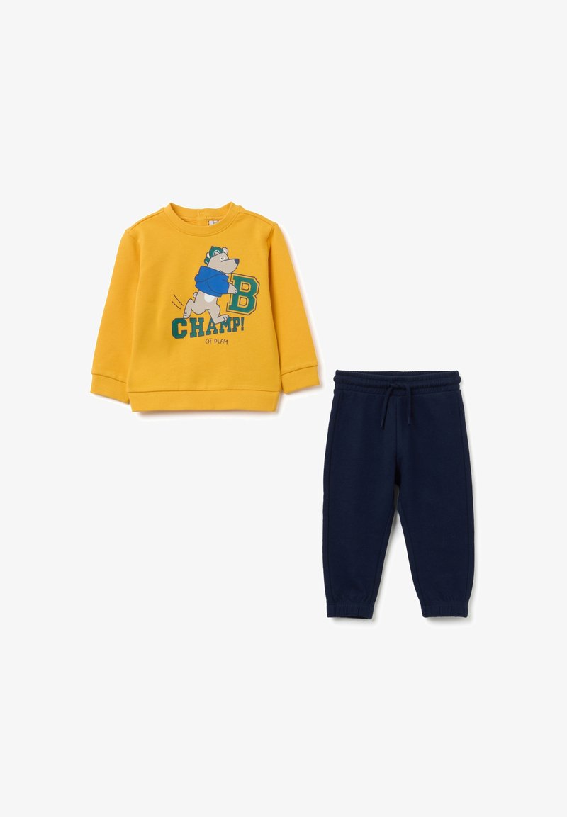 Geel sweatshirt met een beerafbeelding en groene tekst, gecombineerd met marineblauwe joggers met een elastische tailleband. Zacht katoen.