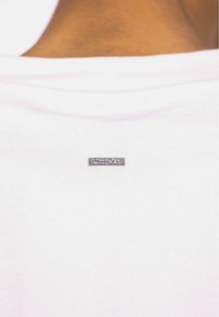 White cotton T-shirt with a ribbed neckline, featuring a small silver brand tag at the back. The fabric appears smooth and soft.