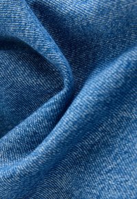 Džinsu audums dažādās zilās krāsas toņos ar izsmalcinātām tekstūras niansēm. Materiāls šķiet mīksts, redzami austie raksti un viegla spīduma nokrāsa.