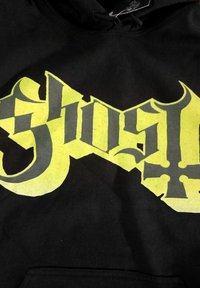 Svart hettegenser med dristig gul grafisk tekst og mørkegrå detaljer, med en stilisert design. Mykt stoff med en lomme foran.
