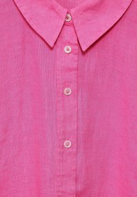 Camicia di lino rosa con colletto classico, placket a sei bottoni con bottoni rotondi e una sottile texture su tutta la stoffa.