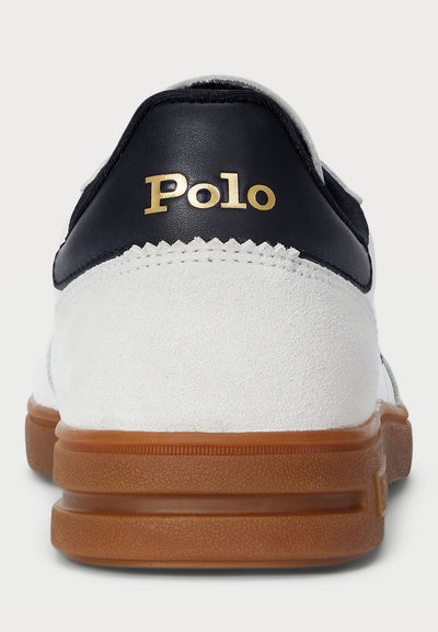 Bijela nubuk tenisica s tamnoplavim kožnim detaljima, s tanjim gumenim potplatima i zlatnim "Polo" brendom na peti.