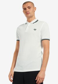 Witte polo met een zwarte gestreepte kraag en manchetten, voorzien van een klein geborduurd logo op de borst. Glad katoen met een fijne textuur.