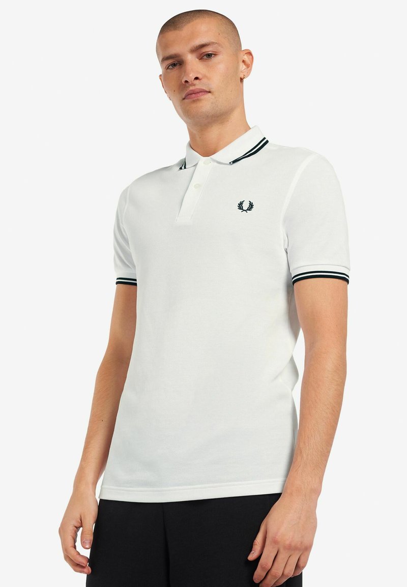 Witte polo met een zwarte gestreepte kraag en manchetten, voorzien van een klein geborduurd logo op de borst. Glad katoen met een fijne textuur.