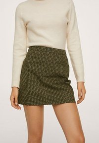 Jupe courte à motifs en vert foncé avec un motif répétitif. Présente une coupe ajustée et une fermeture par bouton à la taille. Haut en tricot doux de couleur crème claire.