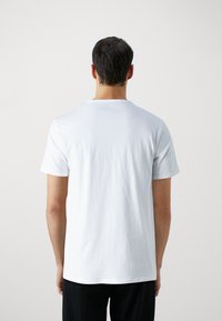 T-shirt en coton blanc à manches courtes et col rond, avec une texture lisse et un design simple, sans ornement.
