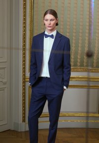 Mornarsko modro krojeno suknjo s slim fit krojem, ki vsebuje belo srajco s gumbi in pisano kravato. Gladko blago in diskretne teksturne podrobnosti.