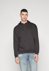 Schwarzer Kapuzenpullover aus weichem Stoff mit_frontlichem Taschen und Kordelzug. Kombiniert mit hellblauen, abgetragenen Jeans. Sanfte Textur, lockere Passform.