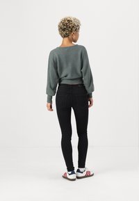 Knitted green sweater with wide sleeves, paired with black skinny jeans and white sneakers featuring red and blue stripes.
