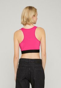 Ružový crop top s čiernym pásom, má dizajn pretekárskeho chrbta a hladkú textúru. Nosený s tmavými džínsovými nohavicami s vysokým pásom.