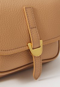 Tan leather handbag with a textured surface, featuring a gold hardware clasp and a stitched strap detail. Smooth, structured shape.