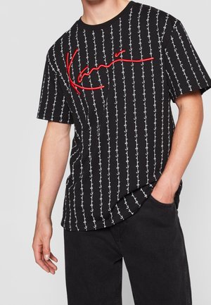 Camiseta negra de algodón con patrón blanco de anclas y logotipo rojo "Kani". Manga corta; ajuste relajado; cuello redondo; textura suave.