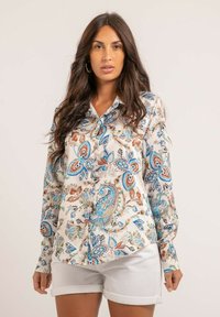 Blouse à manches longues en tissu léger, ornée d'un motif floral et paisley multicolore avec des tons de bleu, marron et crème. Fermeture à boutons à l'avant et col.