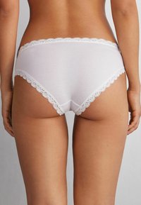 Witte katoenen slipjes met een geschulpte kantafwerking aan de taille. Gladde textuur, eenvoudig ontwerp en een middelhoge snit.