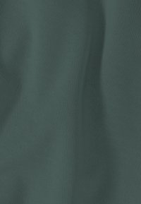 Zachte groene stof met een subtiel ruitvormig doorgestikt patroon en zachte plooien die licht- en schaduwwerking creëren.