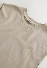 Beige crew neck t-shirt laid flat with a small embroidered sun design on the chest and a visible NEXT brand label inside collar.