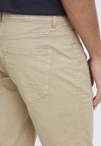 Beige pamut chino nadrág egyenes szabásban, hátul díszvarrott zsebbel és a zseb felett található márkacímmel.