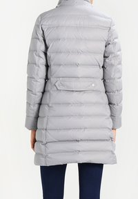 Grå puffet jakke med horisontalt quiltet mønster, trykknaplukning ved kraven og bælte-detail bagpå. Blød, skinnende tekstur.