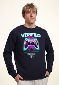 Felpa navy con stampa grafica che presenta un controller di gioco, testo al neon "VERIFICATO" e logo "Precaricato". Tessuto in cotone morbido, collo a giro.