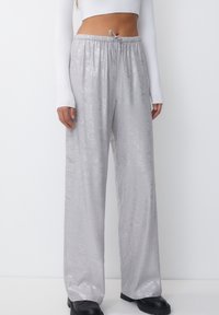 Zilveren wijd beenpantalons met een glanzende textuur en elastische tailleband. Bevat een koord en subtiele patronen. Gepaard met zwarte platformlaarzen.