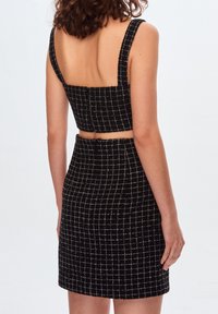 Ensemble top court noir et jupe ajustée avec un motif à carreaux, un tissu structuré, des bretelles larges et une silhouette mi-haute.