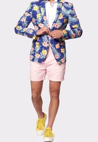 Niebieski żakiet w kwiatowy wzór z różowymi szortami i żółtymi sneakersami. Żakiet wyróżnia się mieszanką tropikalnych kwiatów i liści palmowych.