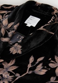 Juodas aksominis chalatas, puoštas šviesiai rožiniu gėlių raštu, su šalikiniu color ir minkšta tekstūra. Etiketėje užrašyta "KITAS kartas svajoti."