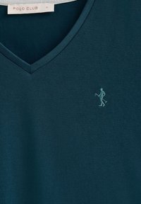 T-shirt teal à col en V en tissu doux, ornée d'une petite figure brodée avec un maillet, marquée "POLO CLUB" sur l'étiquette.