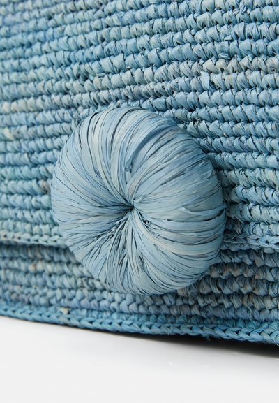 Woven blue bag with a textured surface. Features a large, round, matching button closure made of similar material and color.