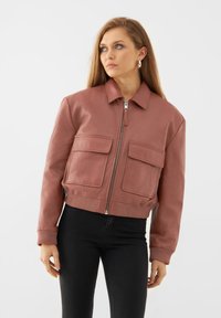 Giubbotto bomber in pelle color rosa con colletto, zip frontale e due grandi tasche a toppa. I polsini e l'orlo a costine aggiungono texture.